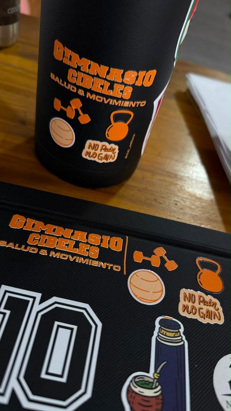 Stickers de identidad de Gimnasio Cibeles aplicados sobre una botella y un bolso